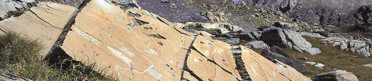 Vue rapprochée de certaines gravures rupestres de la Vallée des Merveilles, avec des figures symboliques tracées sur de grandes dalles de pierre au cœur d’un paysage alpin rocheux. Archives APAM. Fin de la description de l’image.