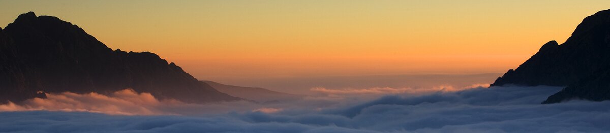 Vue depuis le Col de Fremamorta, avec une mer de nuages remplissant la vallée entre les montagnes sombres et le ciel doré à l’horizon. Archives APAM. Fin de la description de l’image.